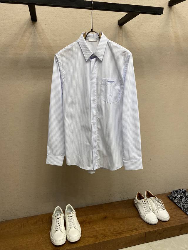 Dior，23Ss新款衬衫将考究剪裁与运动精神结合，全新演绎衣橱里的主打单品。采用白色棉府绸精心制作，饰以蓝色条纹，别致的结构、胸前饰以蓝色 Christian
