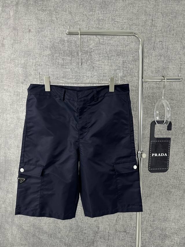 普拉达2024新款金属三角标男士尼龙口袋三角标识短裤 这款三角形织物徽标装点的男士百慕大短裤源于re-Nylon再生尼龙项目。Re-Nylon 再生尼龙系列是